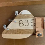 Front view of 3 string guitar with wooden headstock and leather strap