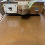 Side view of the bottom of the H_UPMANN CBG, showing the output jack, wine bottle volume knobs, and one chrome strap button of the H_UPMANN cigar box guitar by Bob.