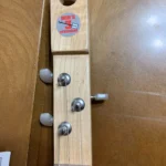 The image shows the headstock of a wooden guitar with three tuning pegs and a sticker labeled "Bob's 3 Stringers."