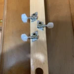 The image shows the headstock of a wooden guitar with three tuning pegs