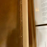 Close-up of a guitar neck with white side markers and Roberts screw fret markers, resting on a wooden surface. Chord diagrams are partially visible nearby.