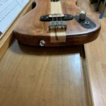 Solid body guitar resting on a piano, with sheet music in the background. The guitar features a laminated wood body, maple neck, and chrome hardware.