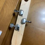The image shows the headstock of a wooden guitar with three tuning pegs