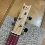 Front view of 3 string guitar with wooden headstock and leather strap