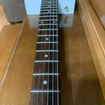 Close-up of the neck: Maple neck with walnut wood fretboard, oak heel, plastic inlay fret markers, plastic inlay side dot markers, adjustable hard tail bridge, 6 steel wound string tuned EADGBE all part of the 6 String Guitar by Bob's 3 Stringers.